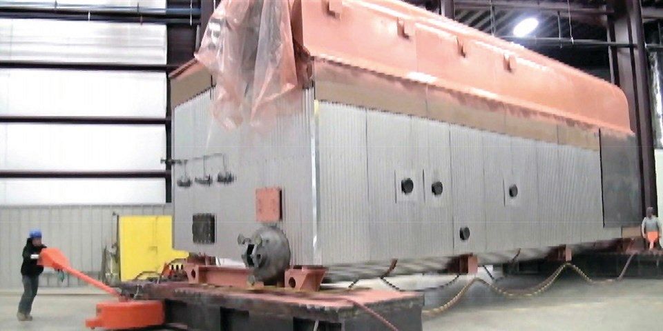 Two operators move a new 100-ton boiler from bay-to-bay in a manufacturing facility.
